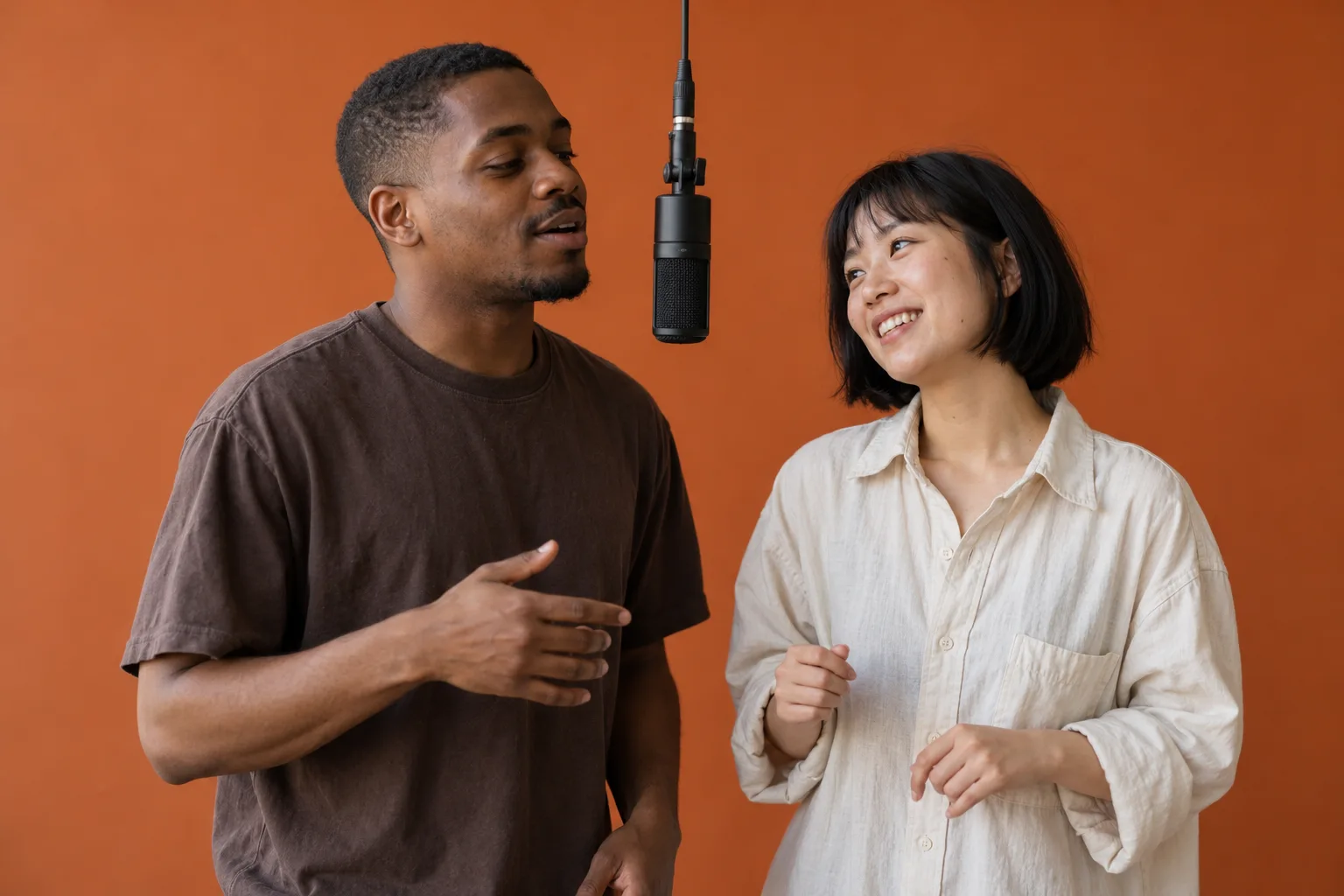 Two fictional friends at a hanging microphone against a matte orange backdrop